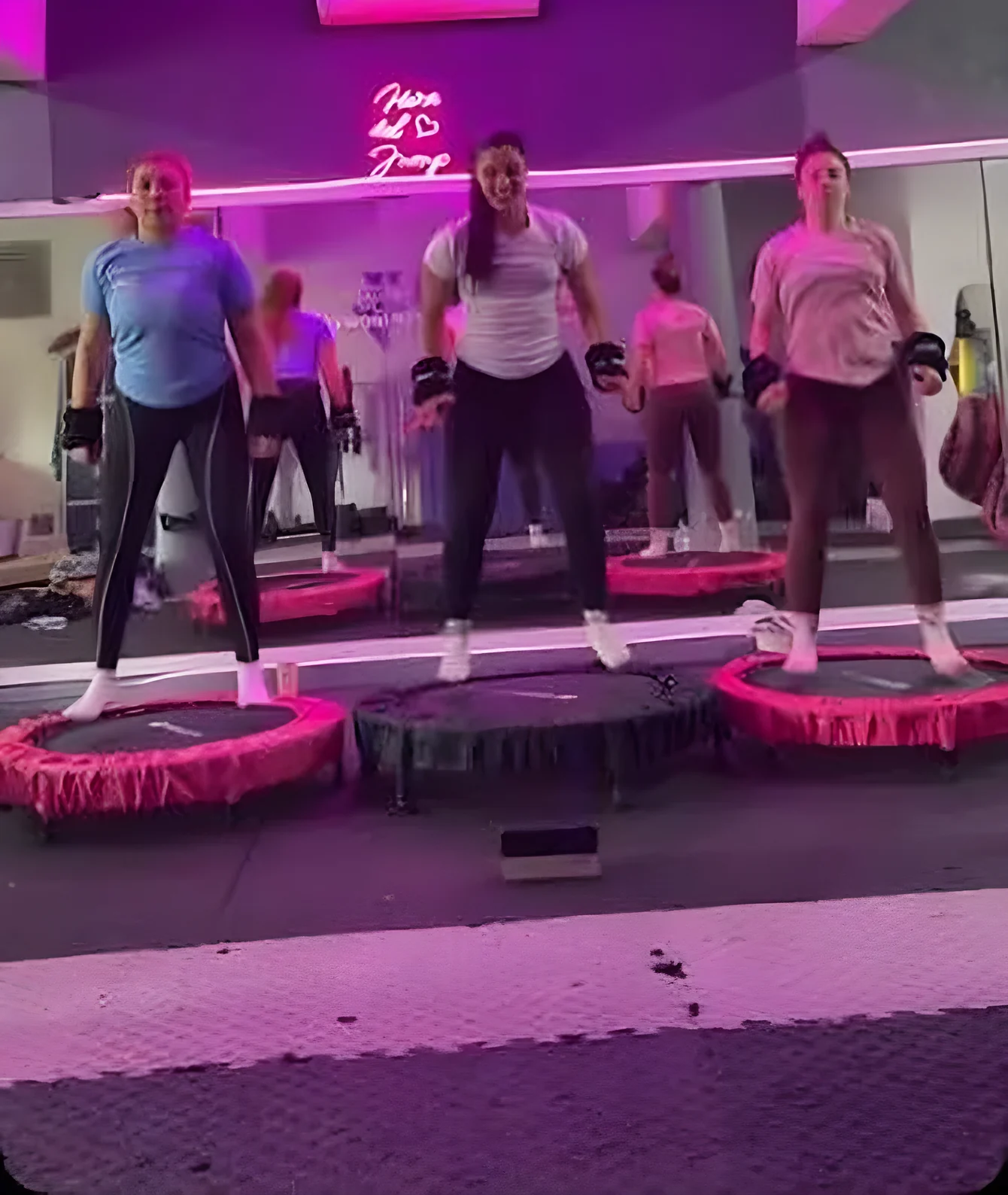 Alumnas saltando en mini camas elásticas rosadas durante una clase de Jump Fit con luces neón